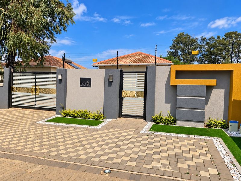 Modern front facade featuring a secure boundary wall, electric fencing, paved driveway, and dual access gates with contemporary architectural detailing.