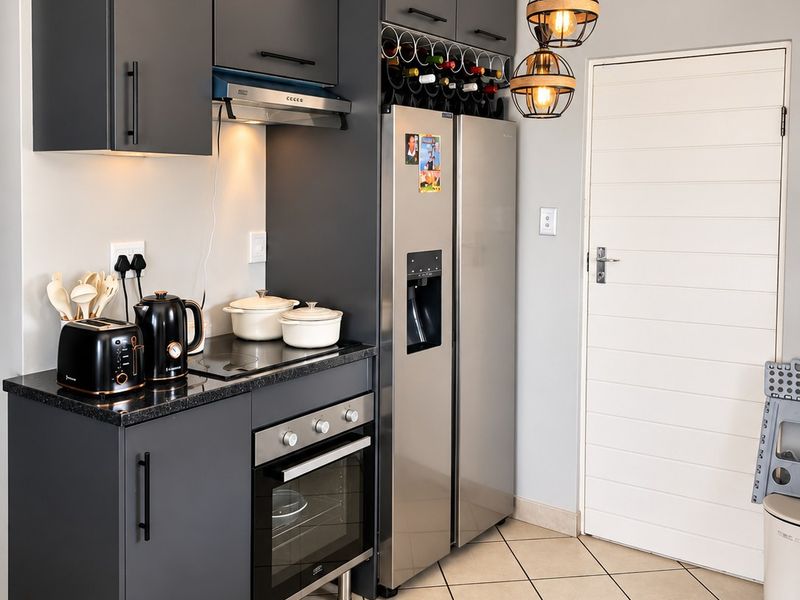 Modern kitchen featuring dark grey cabinetry, built-in oven, extractor fan, integrated wine rack, and neutral tiled flooring.