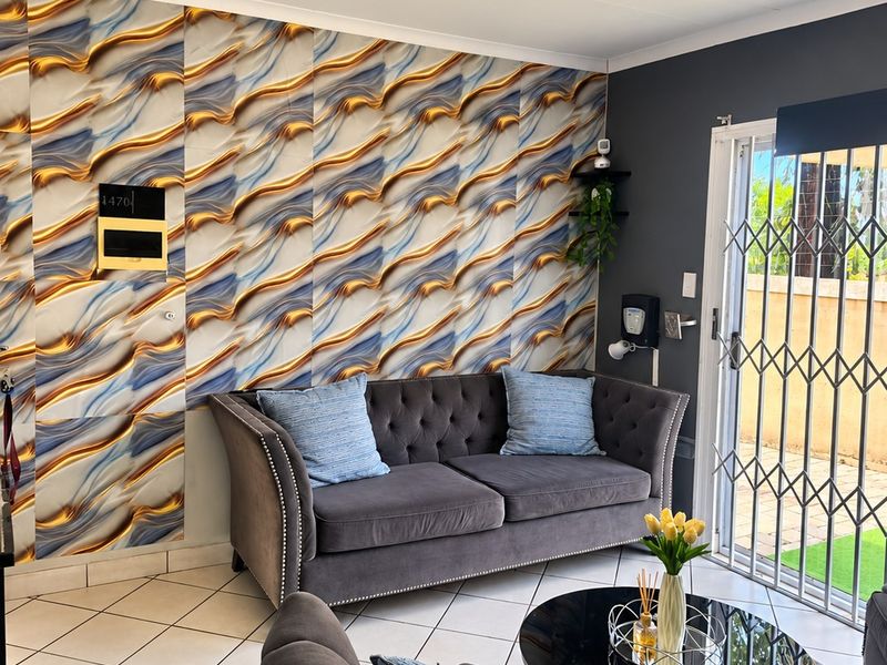 A well-maintained living room featuring tiled flooring, a decorative feature wall, and a sliding glass door with a security gate leading to the exterior.