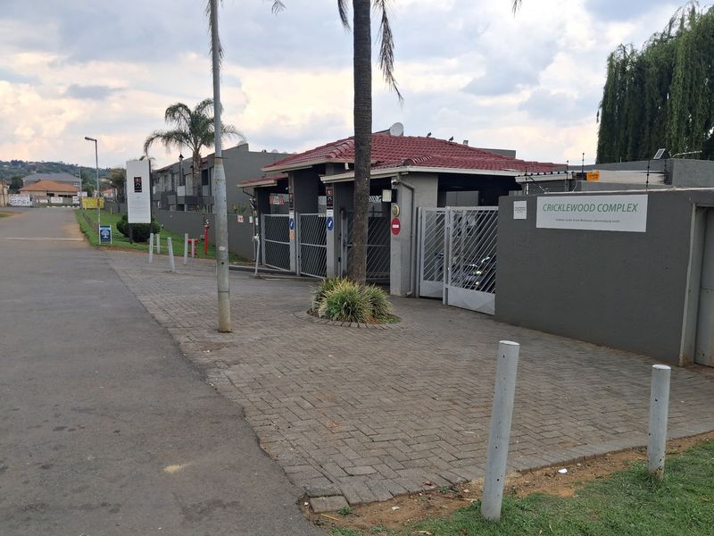 Front entrance view of Cricklewood Complex featuring a paved driveway, secure gated access, and perimeter wall with electric fencing.