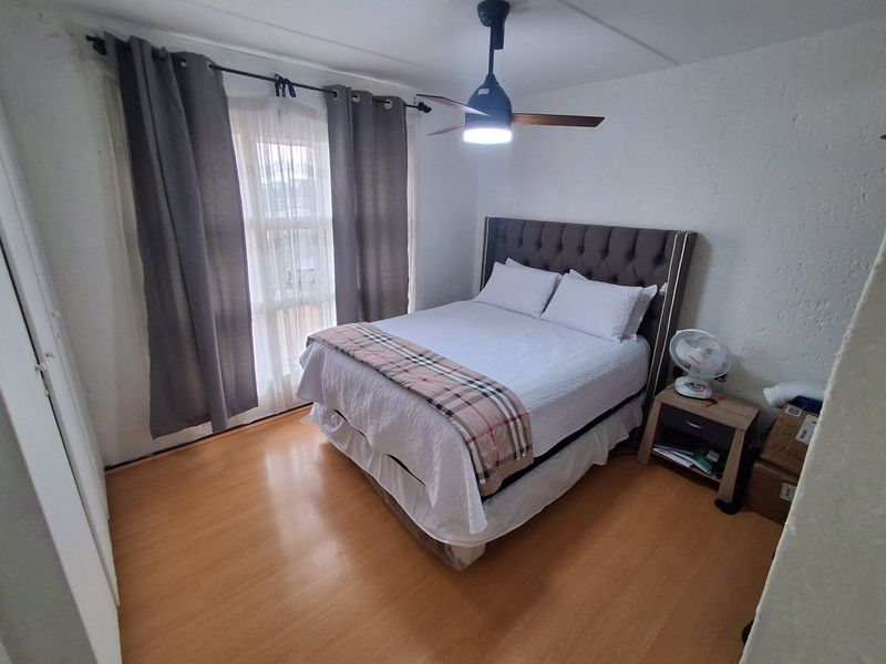 A bedroom featuring laminate flooring, a ceiling fan, and a built-in cupboard, providing a functional and comfortable sleeping space.