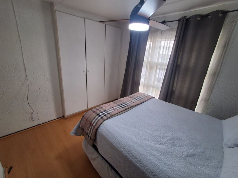 A bedroom featuring laminate flooring, built-in cupboards, and a ceiling fan, with visible wall texture and window treatments.