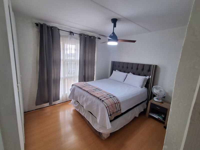 A functional bedroom featuring laminate flooring, a ceiling fan with integrated lighting, and a built-in wardrobe.