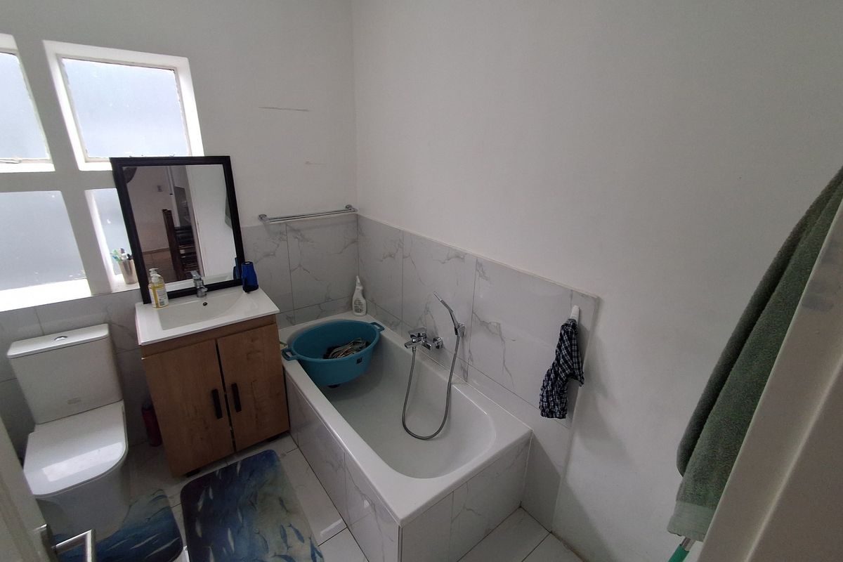 A functional bathroom featuring a vanity cabinet, basin, toilet, and a bathtub with a shower mixer, finished with tiled flooring and splashbacks.