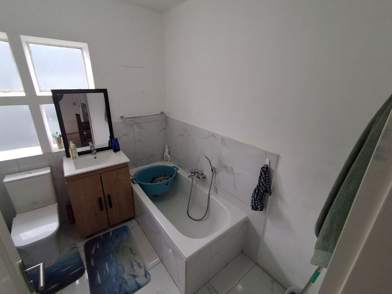 A functional bathroom featuring a vanity cabinet, basin, toilet, and a bathtub with a shower mixer, finished with tiled flooring and splashbacks.