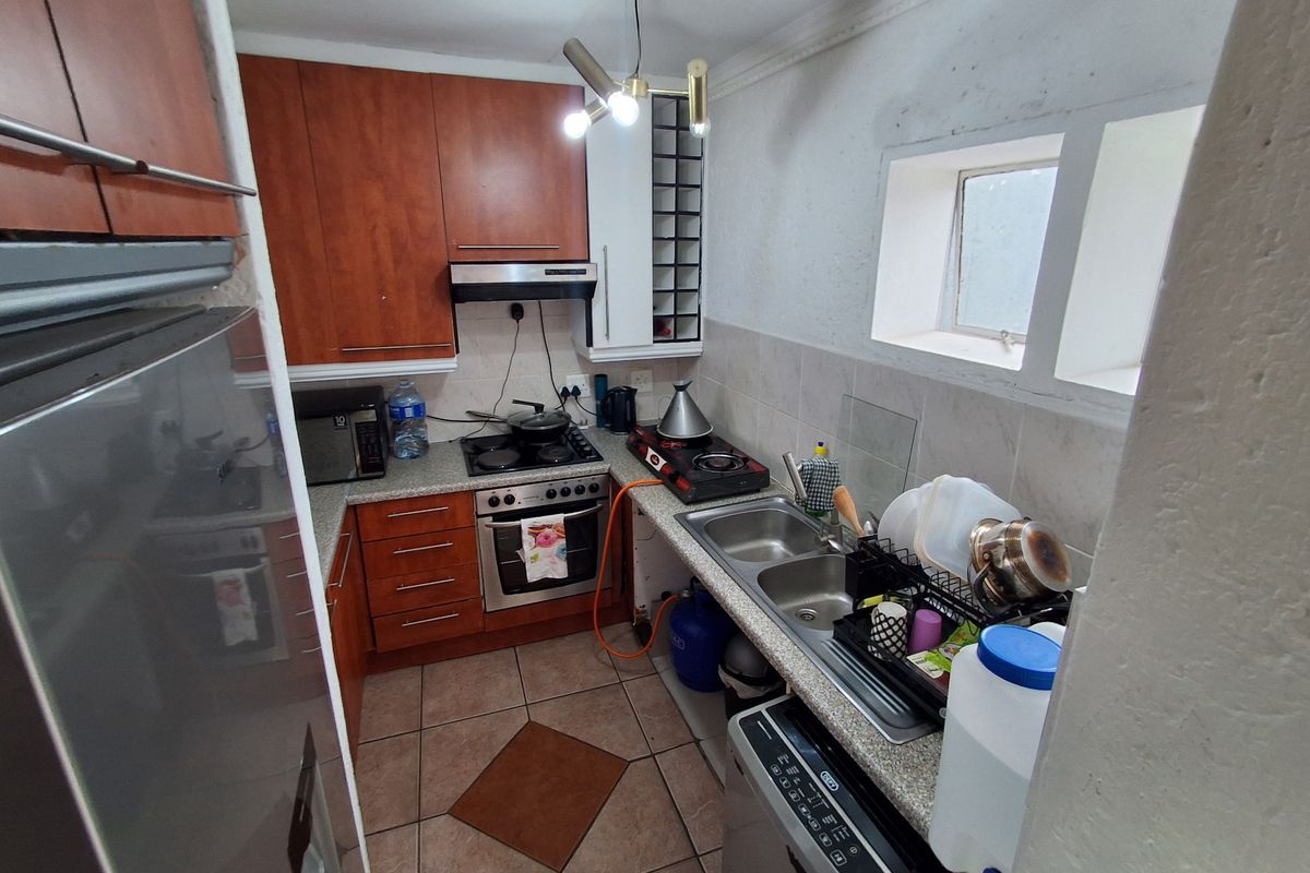 Compact kitchen featuring wooden cabinetry, double sink, built-in oven, and extractor fan with tiled flooring and backsplash.
