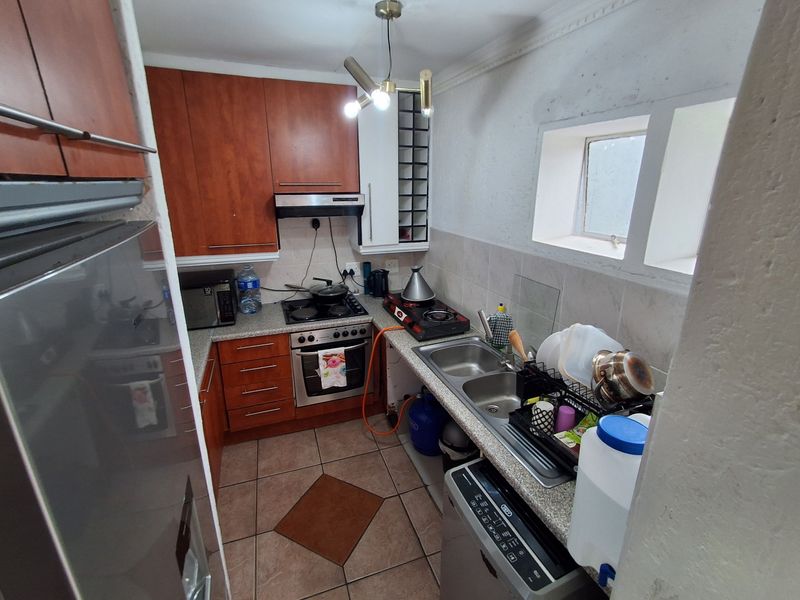Compact kitchen featuring wooden cabinetry, double sink, built-in oven, and extractor fan with tiled flooring and backsplash.