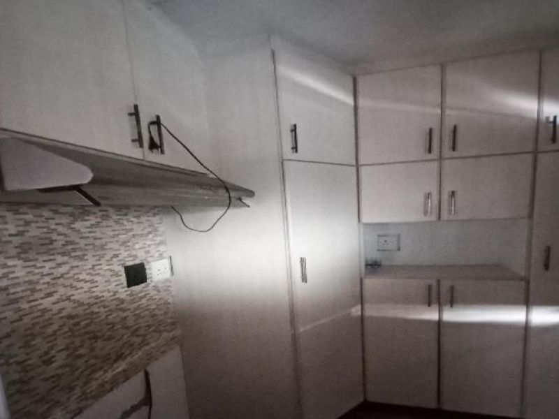 A dated kitchen area featuring built-in cabinetry, a tiled backsplash, and an extractor fan, currently requiring cosmetic updates and improved lighting.