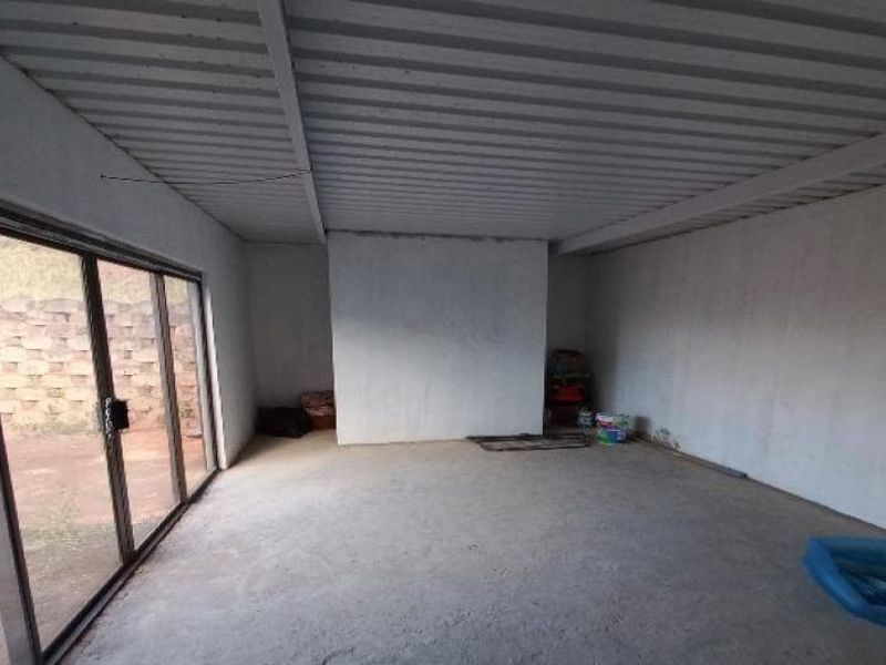An expansive, unfinished covered patio area featuring a corrugated metal ceiling, concrete flooring, and large sliding glass doors leading to the rear garden.
