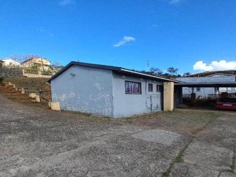 Exterior view of the property featuring a concrete driveway, a carport, and a detached structure with visible exterior wall wear.