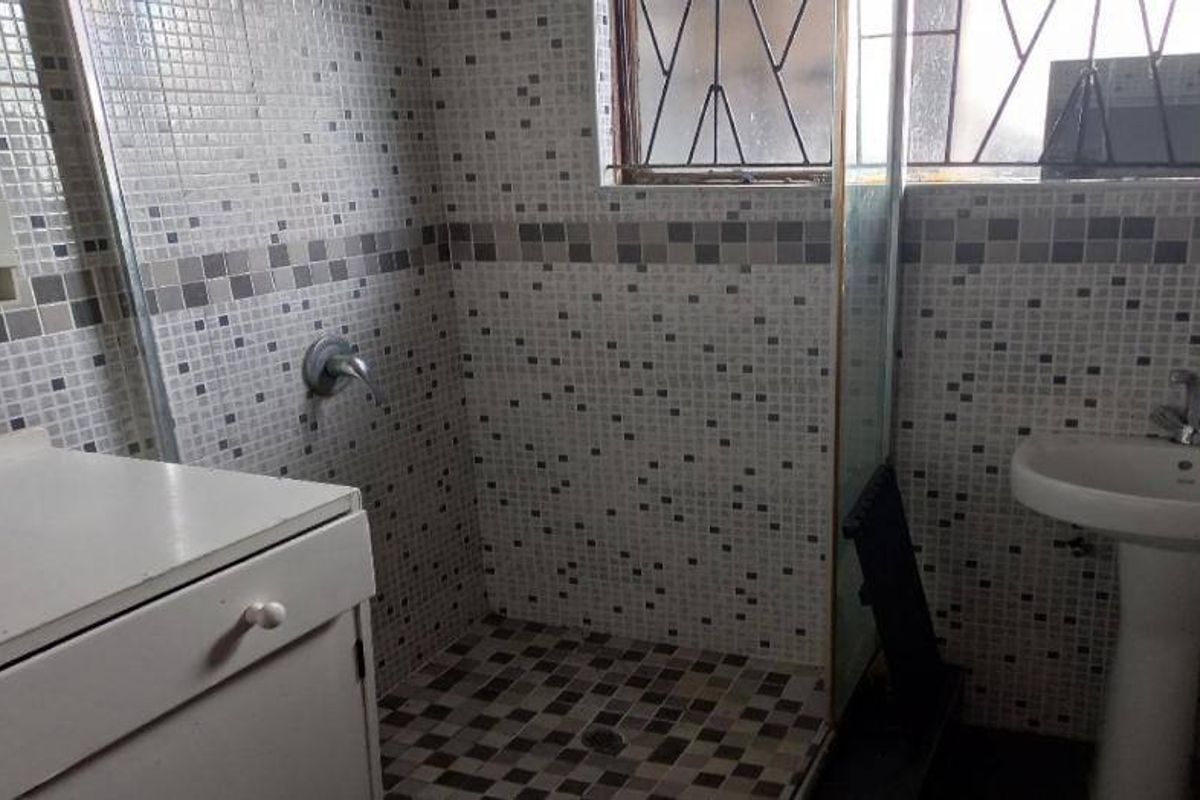 A functional bathroom featuring a pedestal basin, a shower enclosure with mosaic tiling, and a built-in vanity cabinet.