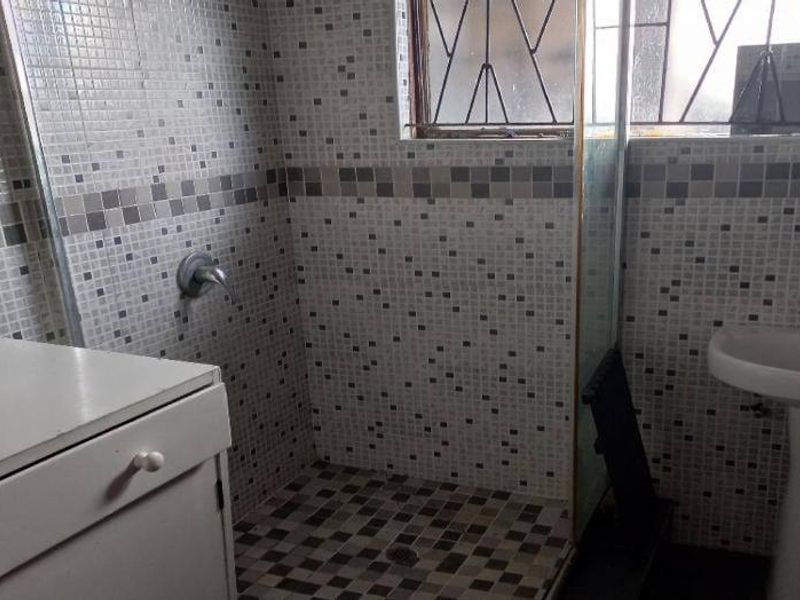 A functional bathroom featuring a pedestal basin, a shower enclosure with mosaic tiling, and a built-in vanity cabinet.