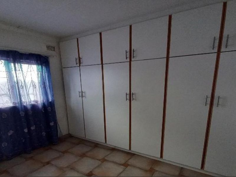 A bedroom featuring extensive built-in cupboards, tiled flooring, and a window fitted with security bars.