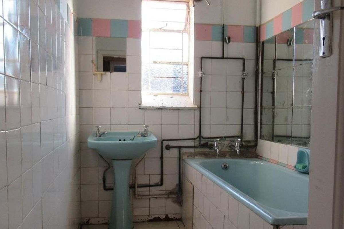 A dated bathroom featuring a blue pedestal basin and matching bathtub, with exposed plumbing and original wall tiling in need of renovation.