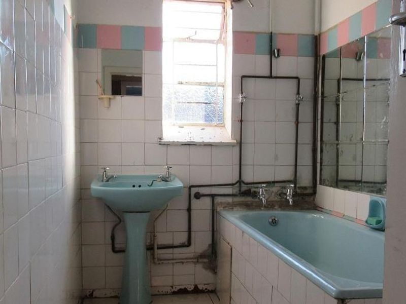 A dated bathroom featuring a blue pedestal basin and matching bathtub, with exposed plumbing and original wall tiling in need of renovation.