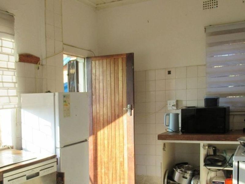 A functional kitchen area featuring tiled splashbacks, a stainless steel sink, and timber door access, currently showing signs of age and wear.