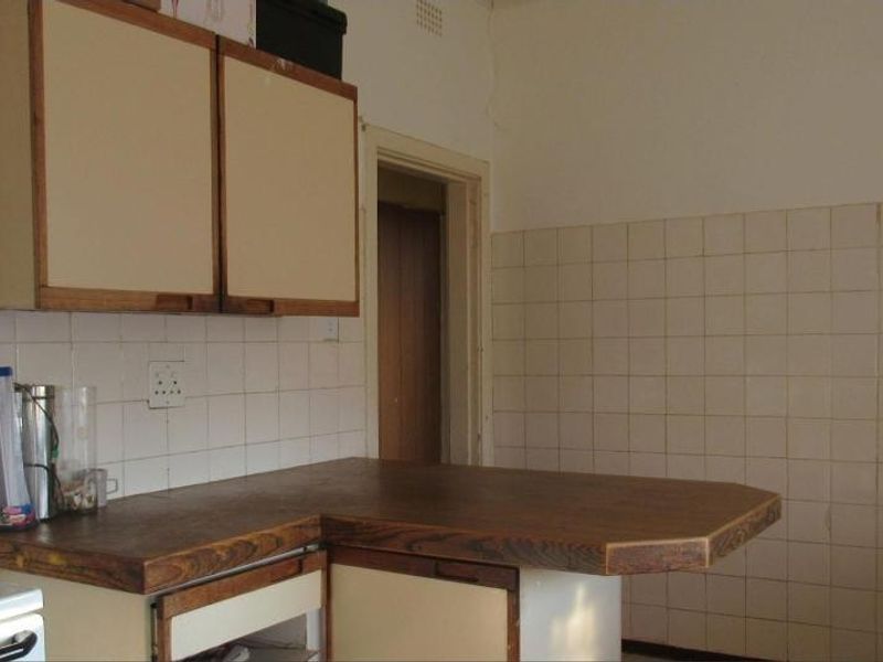 A dated kitchen featuring original cabinetry, tiled splashbacks, and a laminate countertop, offering significant potential for a modern renovation.