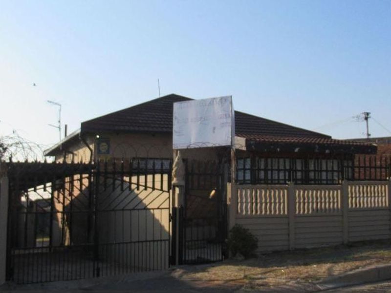 Front exterior view of a single-story house featuring a tiled roof, perimeter precast concrete walling, and metal security gate with razor wire.