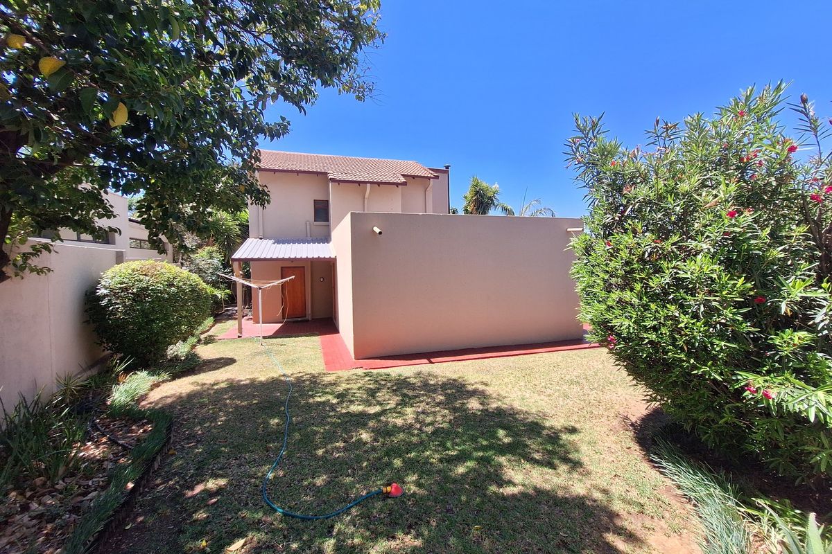A view of the rear exterior of the townhouse, featuring a private garden, concrete patio area, and tiled roof structure.
