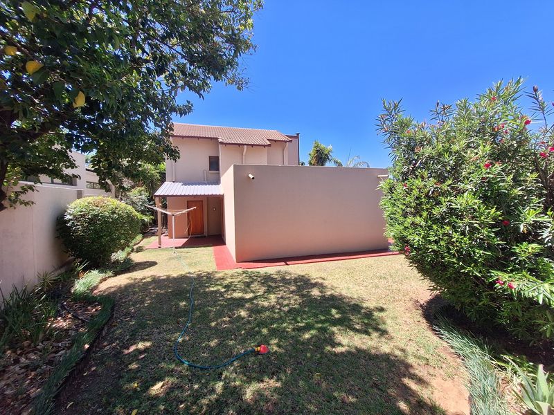 A view of the rear exterior of the townhouse, featuring a private garden, concrete patio area, and tiled roof structure.