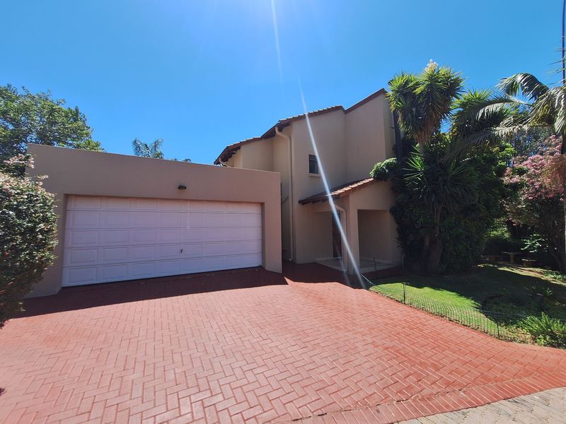 Front view of the townhouse featuring a paved driveway, double garage, and a covered entrance area with established garden surroundings.