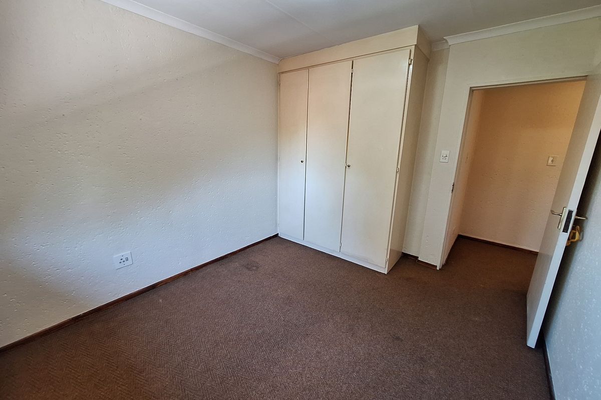 An empty bedroom featuring a built-in wardrobe, carpeted flooring, and neutral wall finishes, offering a blank canvas for potential updates.