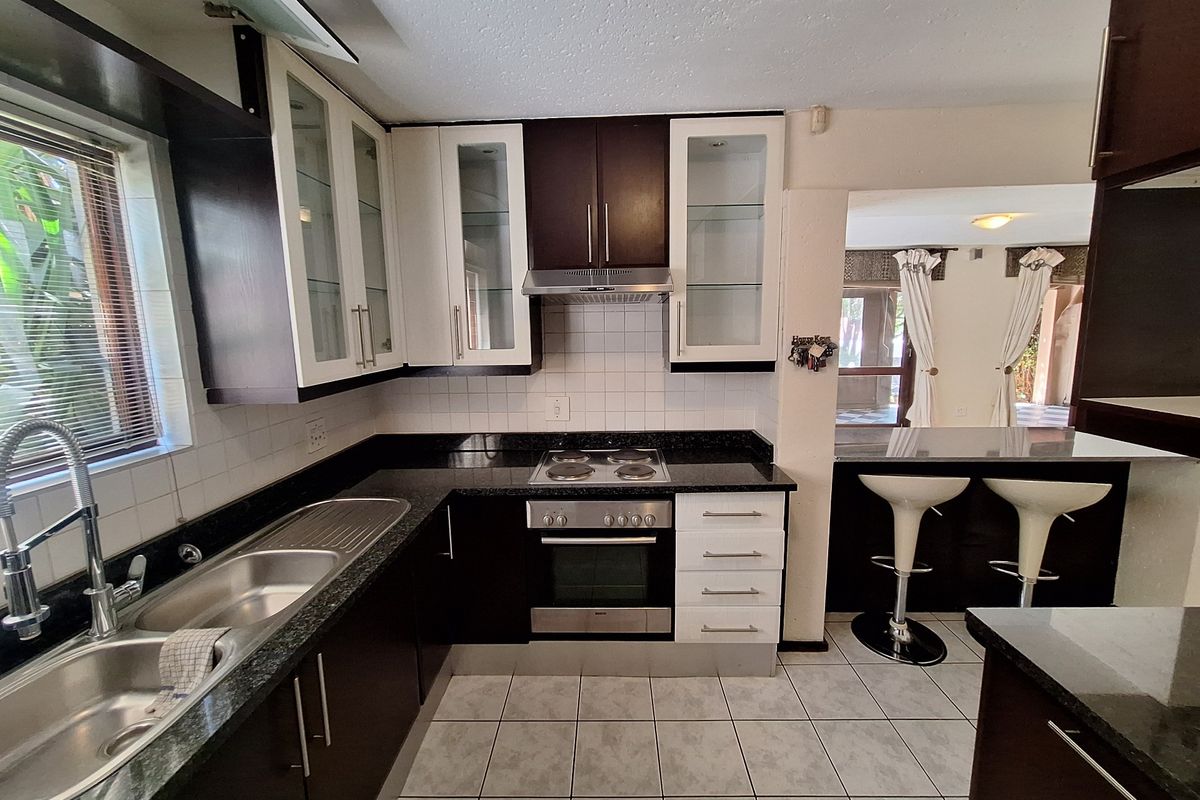 A well-maintained kitchen featuring dark and light cabinetry, granite countertops, integrated appliances, and a breakfast bar overlooking the adjacent living area.