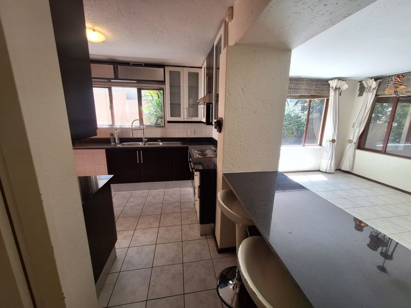 Open plan kitchen and living area featuring dark cabinetry, granite countertops, breakfast bar, and tiled flooring throughout.