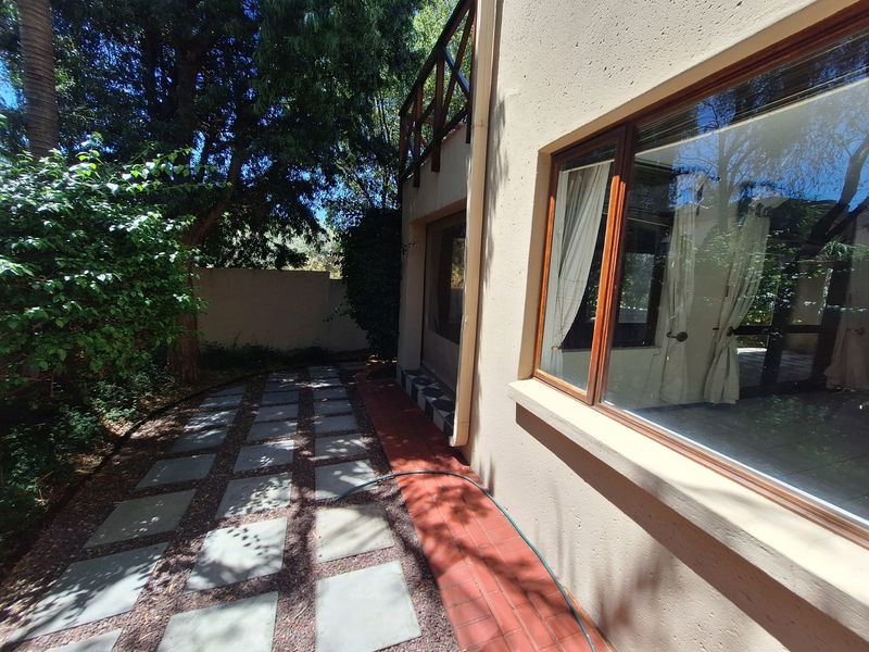 Rear exterior view of the townhouse featuring a paved garden path, timber balcony railing, and large timber-framed windows.