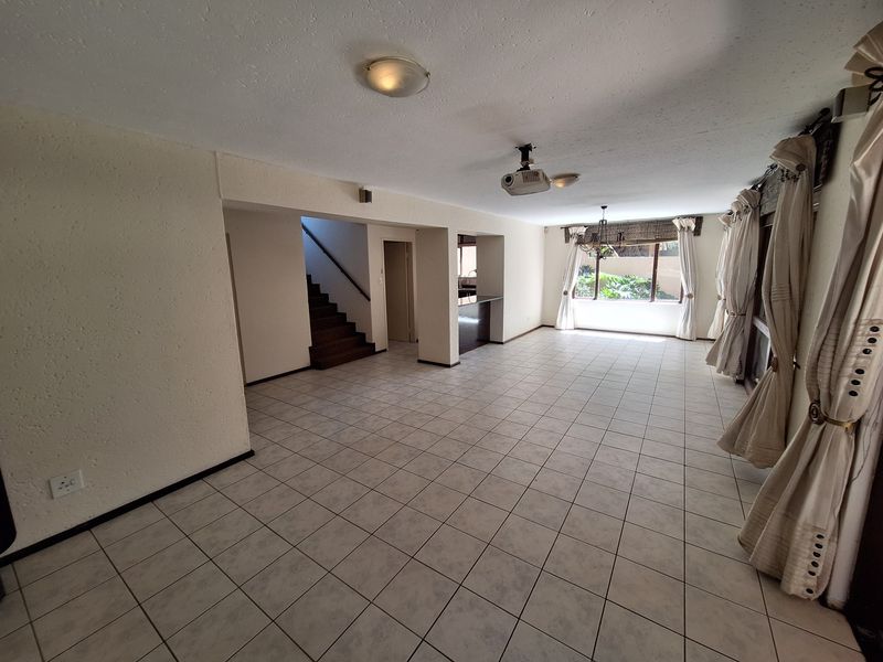Spacious open-plan living area featuring tiled flooring, a staircase, and large windows, offering a versatile layout for modern living.