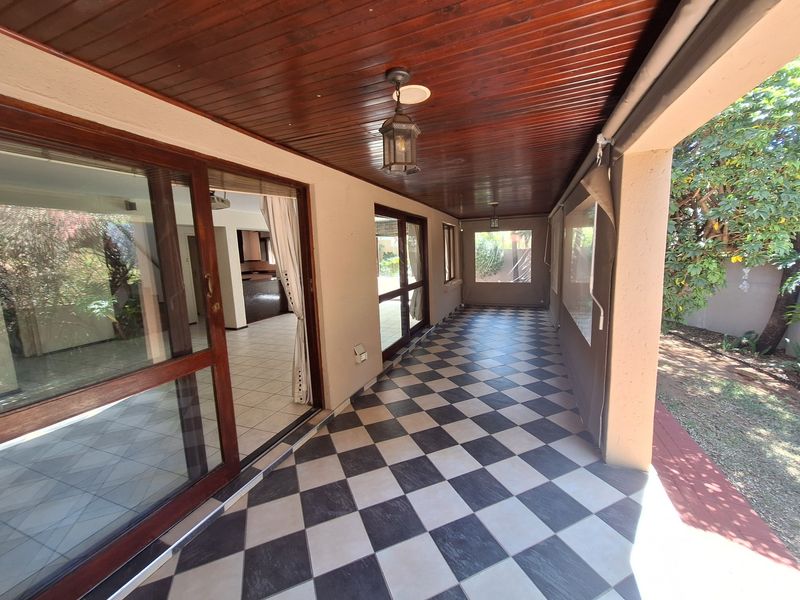 A covered patio featuring a timber-clad ceiling, checkered floor tiles, and sliding glass doors providing seamless access to the interior living space.