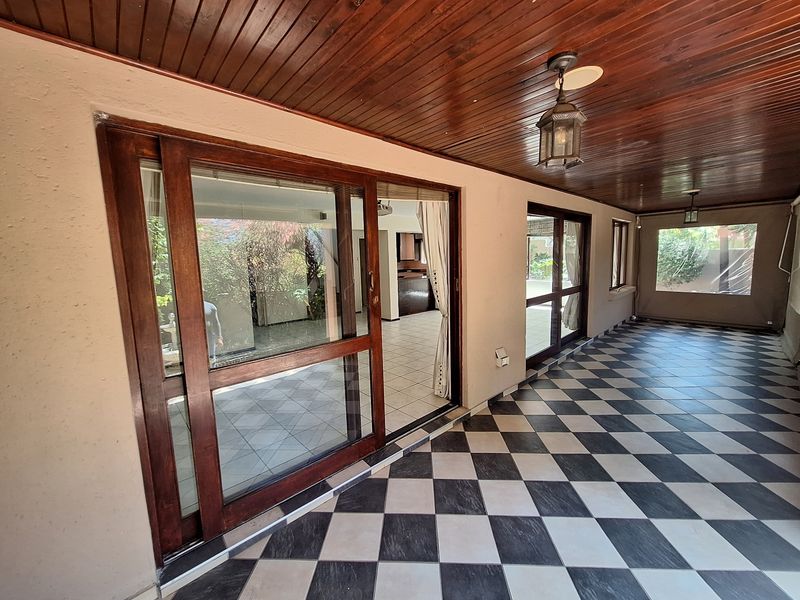A spacious covered patio featuring a timber ceiling, checkered floor tiles, and large sliding glass doors providing seamless access to the interior living area.