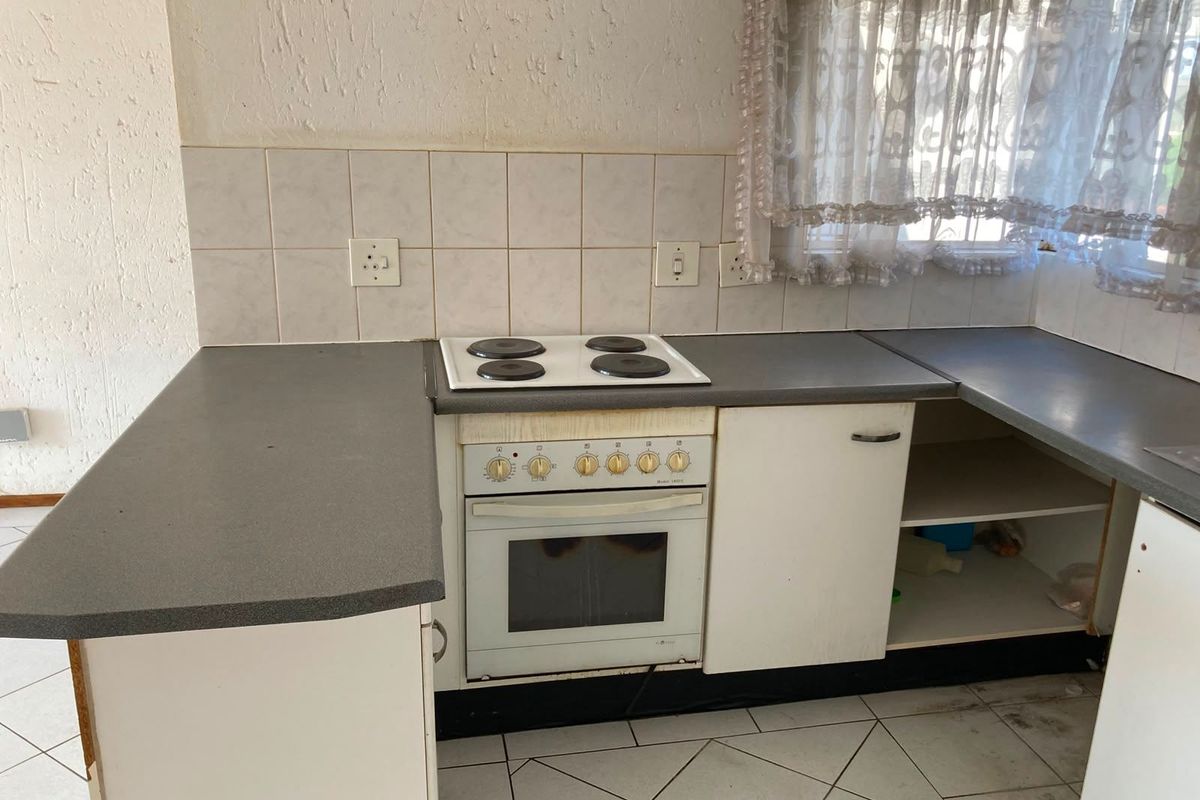 A dated kitchen featuring built-in cabinetry, an electric oven and hob, tiled backsplash, and ceramic flooring, currently in need of cosmetic updates.