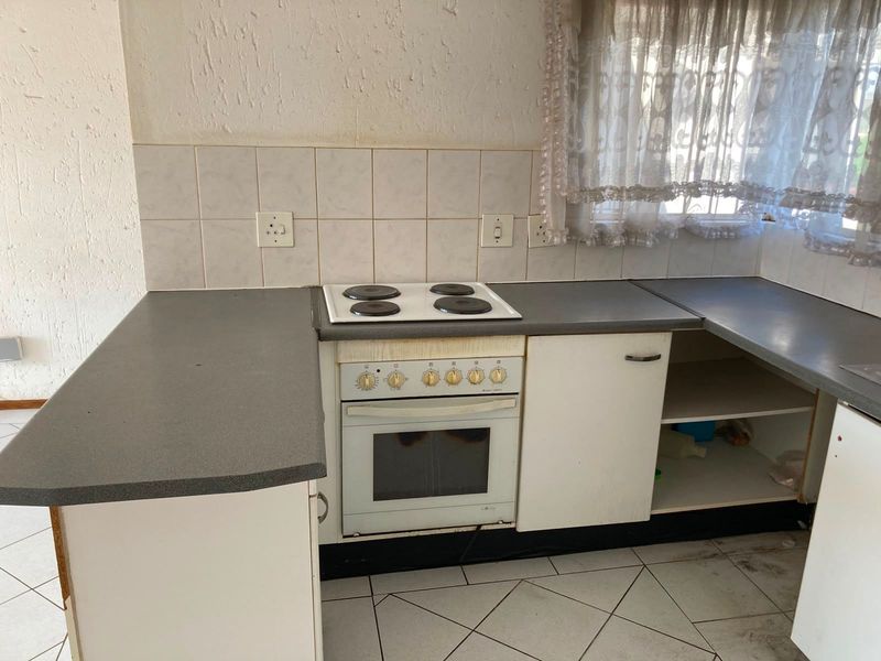 A dated kitchen featuring built-in cabinetry, an electric oven and hob, tiled backsplash, and ceramic flooring, currently in need of cosmetic updates.