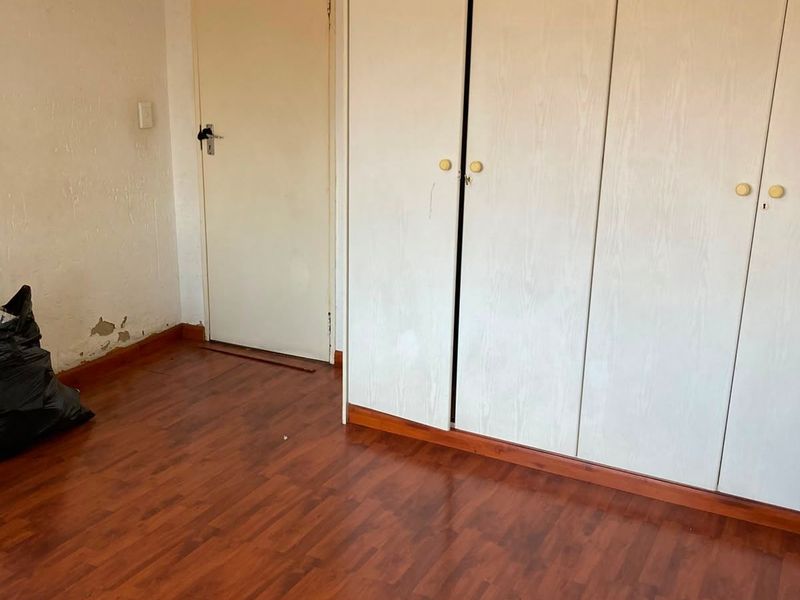 A vacant bedroom featuring laminate flooring and built-in cupboards, requiring minor wall repairs and cosmetic updates.