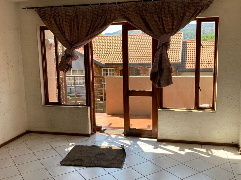 An empty living room featuring tiled flooring and a sliding glass door that opens onto a balcony with neighborhood views.