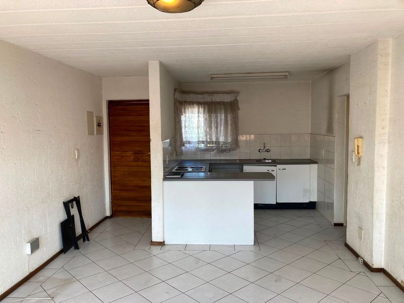 An open-plan living and kitchen area featuring tiled flooring, basic built-in cabinetry, and a functional layout ready for modernization.