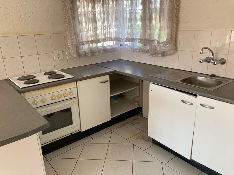 A dated kitchen featuring a built-in oven, electric hob, stainless steel sink, and tiled finishes, currently requiring maintenance and cosmetic updates.