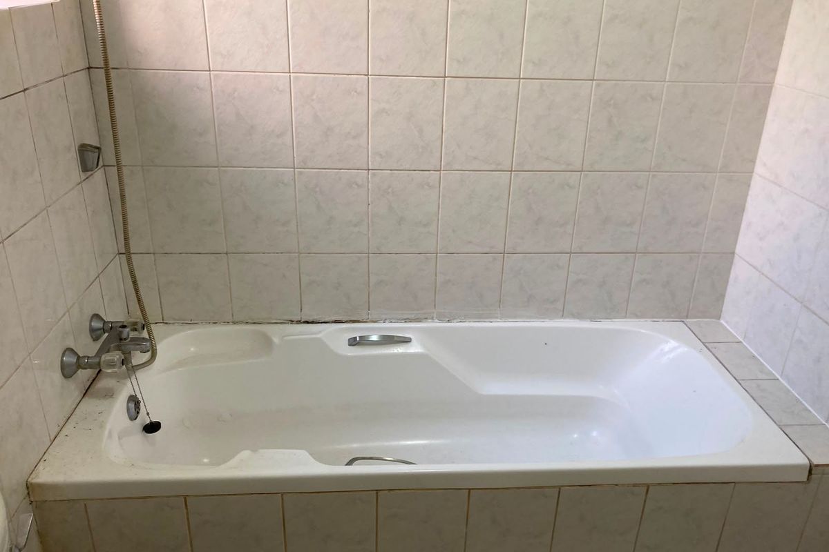 A functional bathroom featuring a built-in bathtub with a handheld shower attachment and tiled wall surrounds, requiring minor maintenance and cosmetic updates.