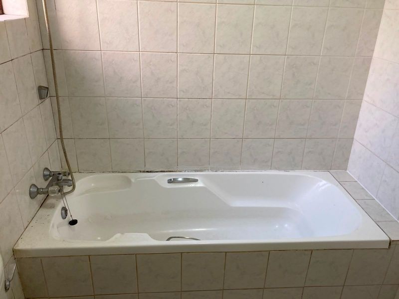 A functional bathroom featuring a built-in bathtub with a handheld shower attachment and tiled wall surrounds, requiring minor maintenance and cosmetic updates.