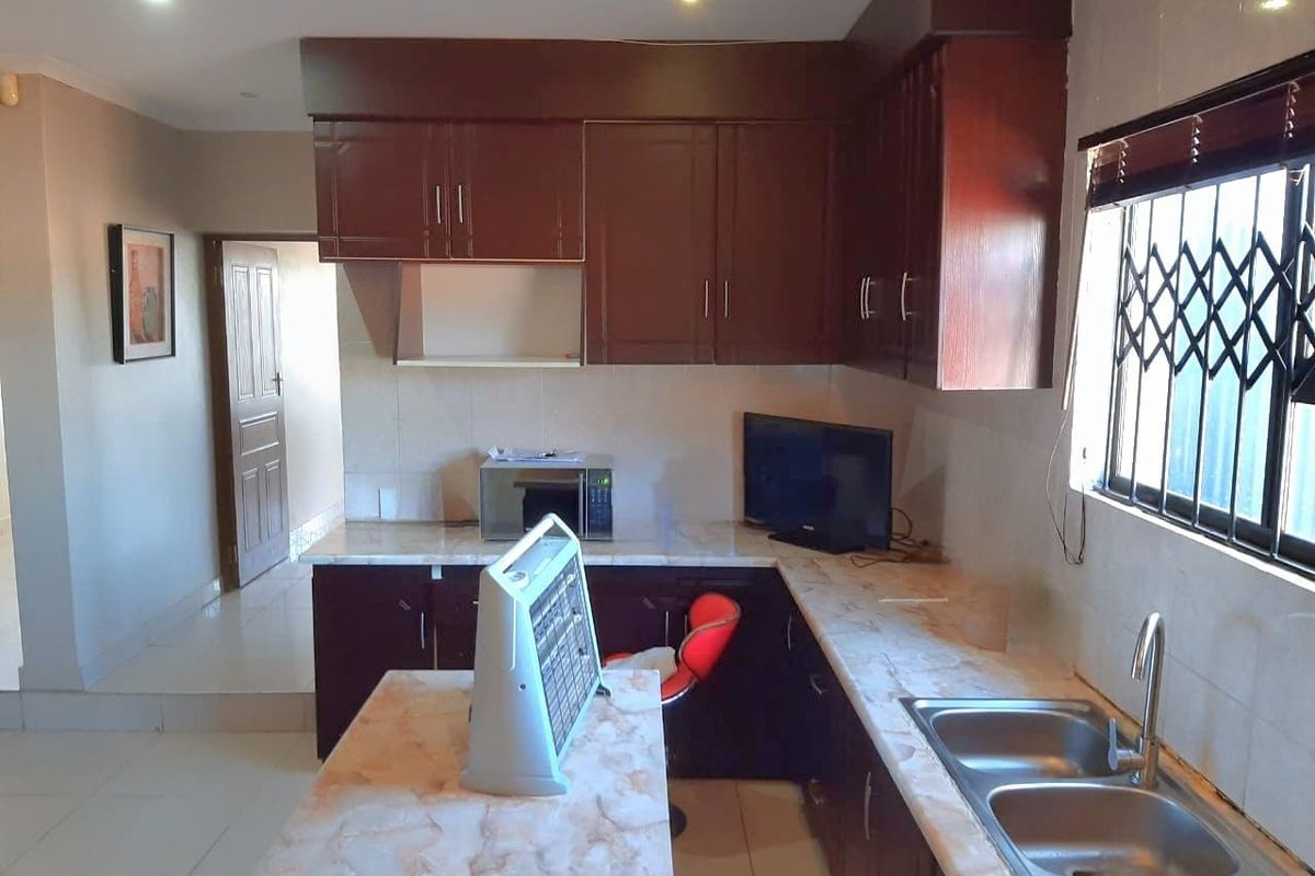 A functional kitchen featuring dark wood cabinetry, laminate countertops, a double bowl stainless steel sink, and tiled backsplash with a window security gate.