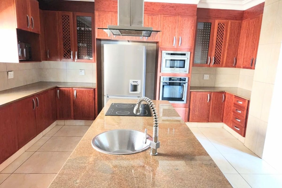 Spacious kitchen featuring a central island with a sink and hob, granite countertops, and extensive wooden cabinetry with built-in appliances.