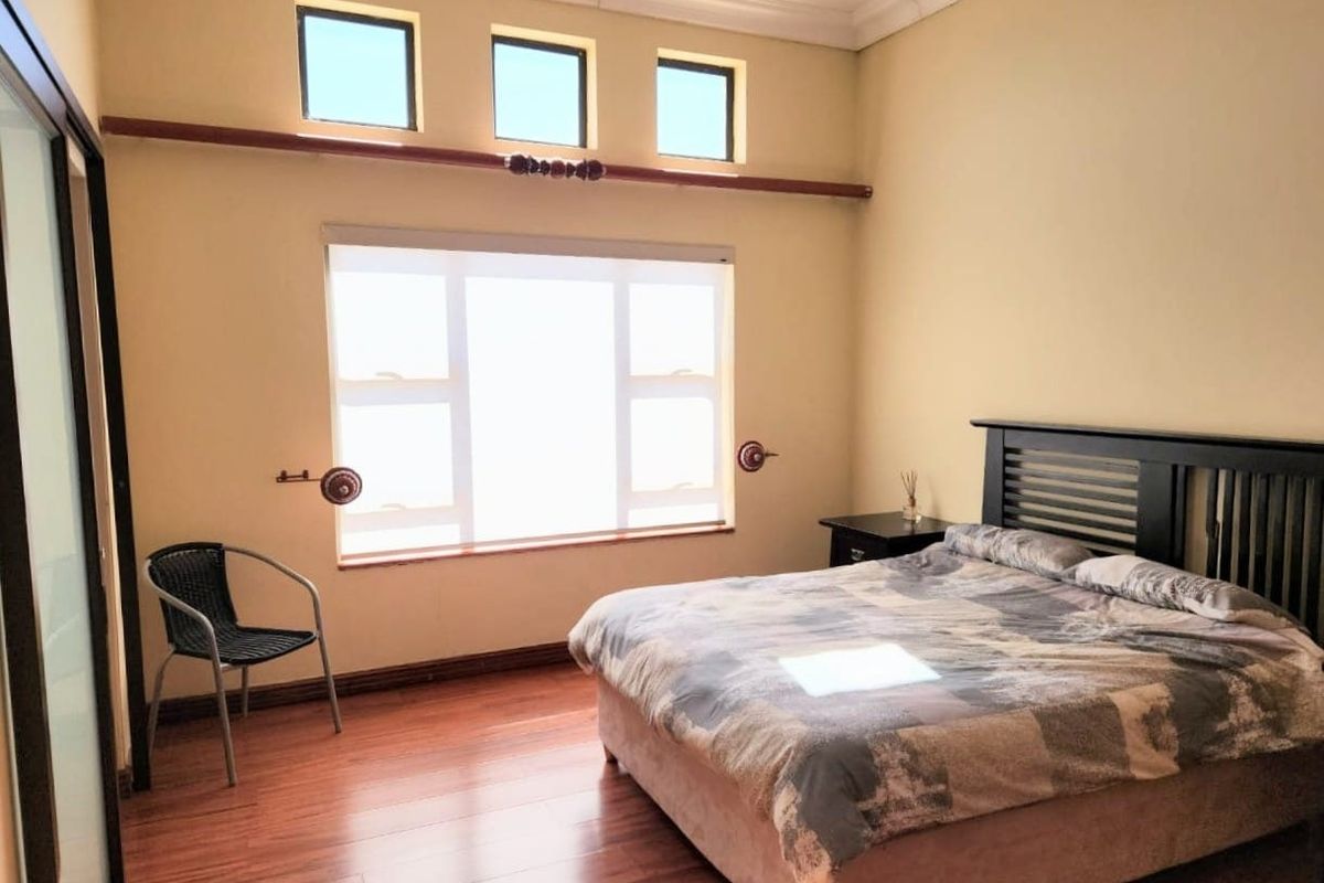 Spacious bedroom featuring laminate flooring, high ceilings with cove cornicing, and ample natural light provided by a large window and additional clerestory windows.