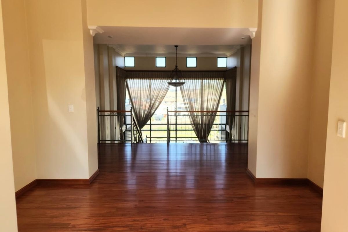 Spacious living area featuring polished hardwood flooring, elegant wrought iron balustrades, and high ceilings with recessed lighting, offering an open and airy atmosphere.