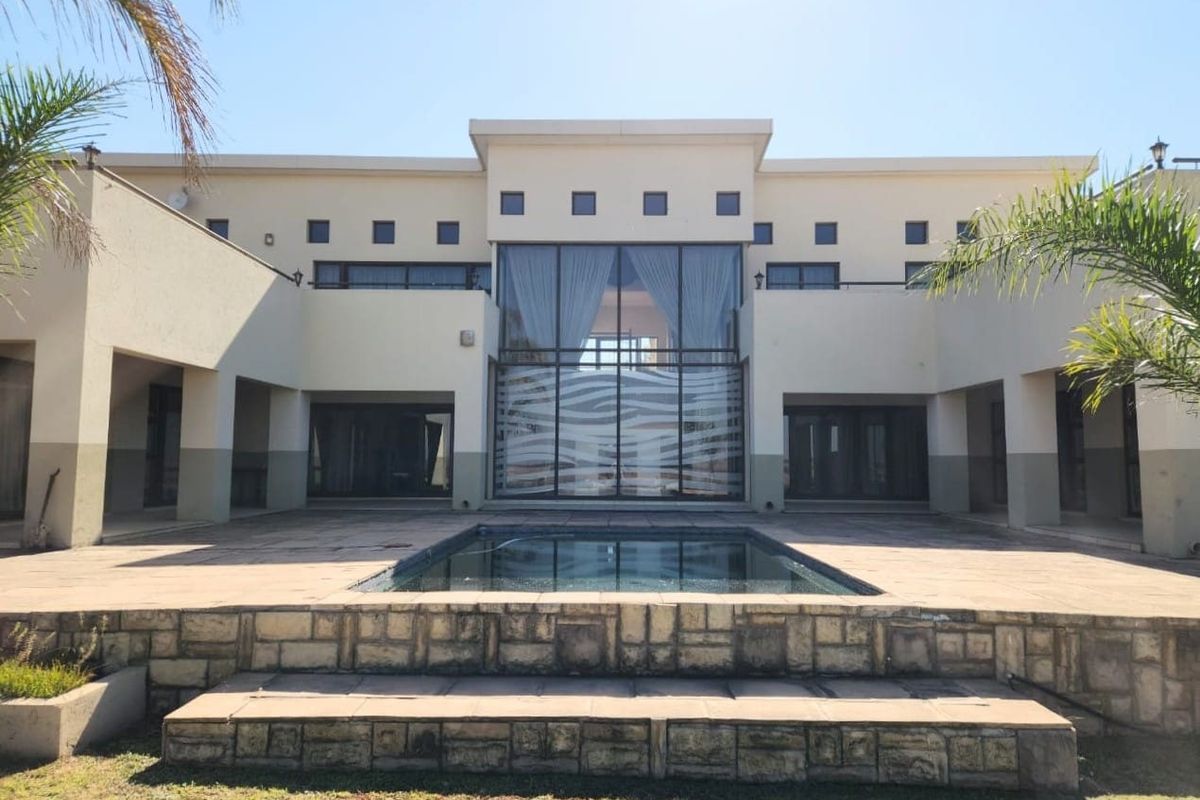 Rear view of a modern residence featuring a swimming pool, stone-clad steps, and a prominent central glass facade with balcony access.