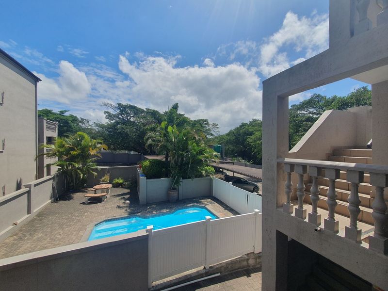 Outdoor communal area featuring a swimming pool, paved patio, and surrounding boundary walls, viewed from an elevated balcony staircase.