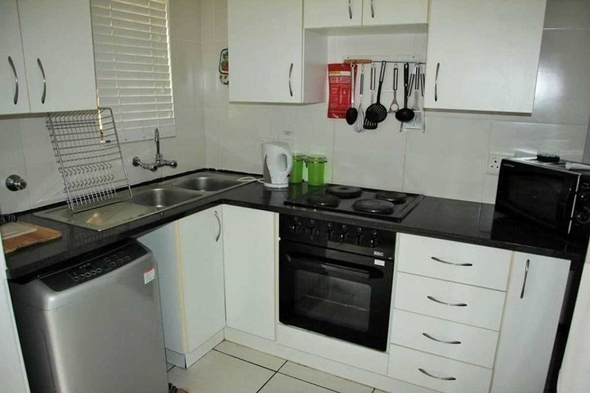 Compact kitchen featuring white cabinetry, dark countertops, a built-in oven with electric hob, and tiled flooring.