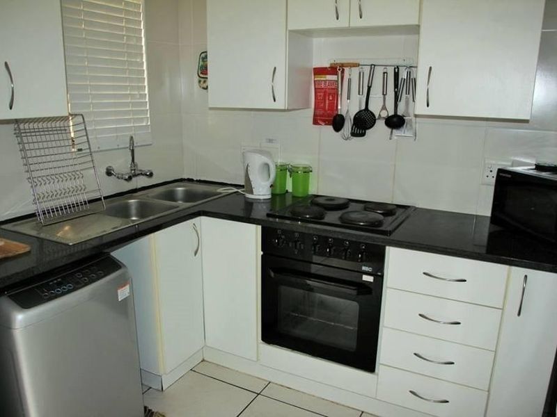 Compact kitchen featuring white cabinetry, dark countertops, a built-in oven with electric hob, and tiled flooring.