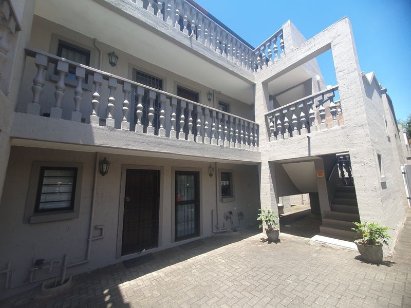 A view of the apartment complex rear courtyard featuring paved flooring, a concrete staircase, and traditional balustrade detailing on the upper level balcony.