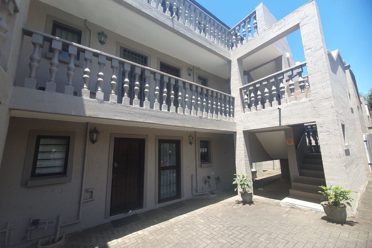 A view of the apartment complex rear courtyard featuring paved flooring, a concrete staircase, and traditional balustrade detailing on the upper level balcony.